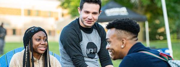 Three students chat amicably while sitting in Adirondack chairs